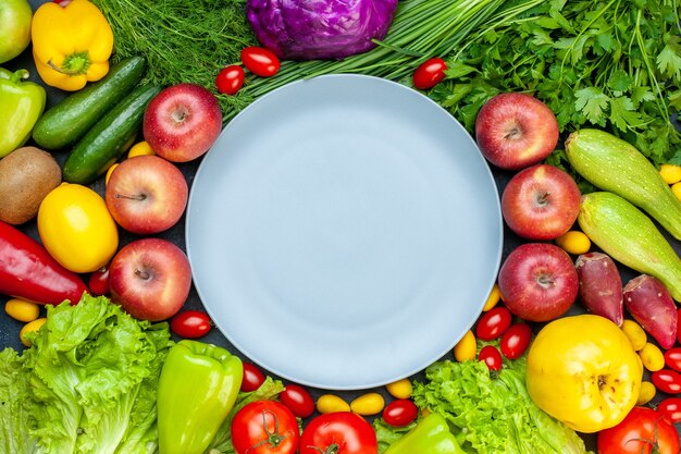 Top view fresh vegetables cherry tomatoes cumcuat radish green onion parsley cucumbers bell peppers apples lettuce red cabbage round plate in center