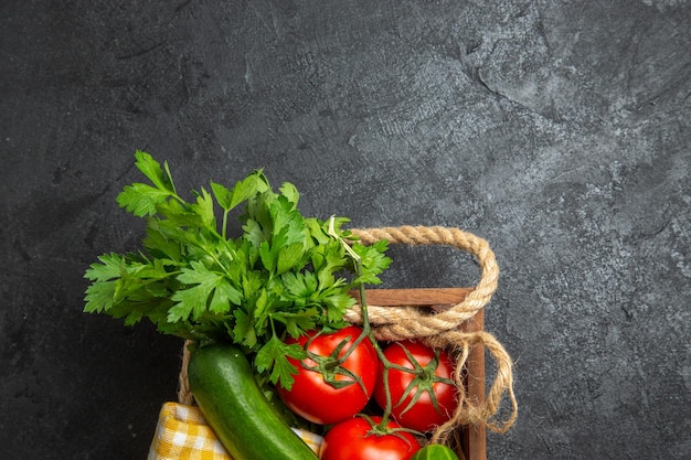 Top view of fresh vegetables red tomatoes cucumbers and squashes with greens on dark grey surface