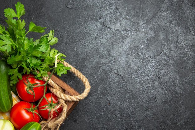 Top view of fresh vegetables red tomatoes cucumbers and squashes with greens on a grey surface