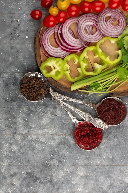 Free photo top view fresh vegetables sliced whole such as onions green bell pepper tomatoes on the grey floor