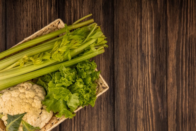 Free photo top view of fresh vegetables such as celery lettuce and cauliflower on a bucket on a wooden wall with copy space