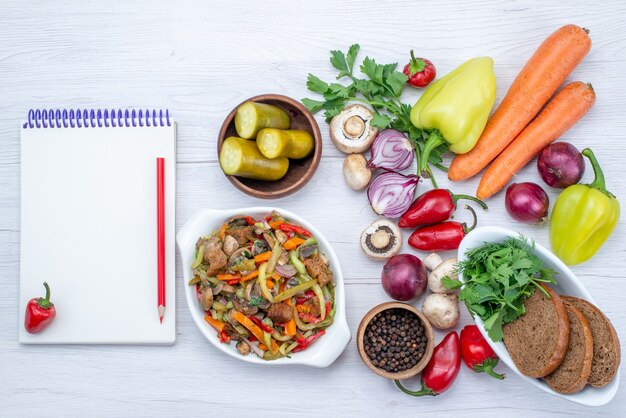 Top view of fresh vegetables such as pepper carrot onions with bread loafs and sliced meat dish on light, vegetable food meal vitamine