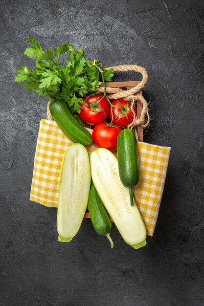 Top view of fresh vegetables tomatoes cucumbers squashes and greens on grey surface