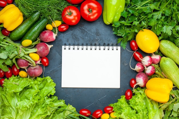 Top view fresh vegetables tomatoes lettuce radish lemon zucchini parsley cherry tomatoes notepad in center on dark surface