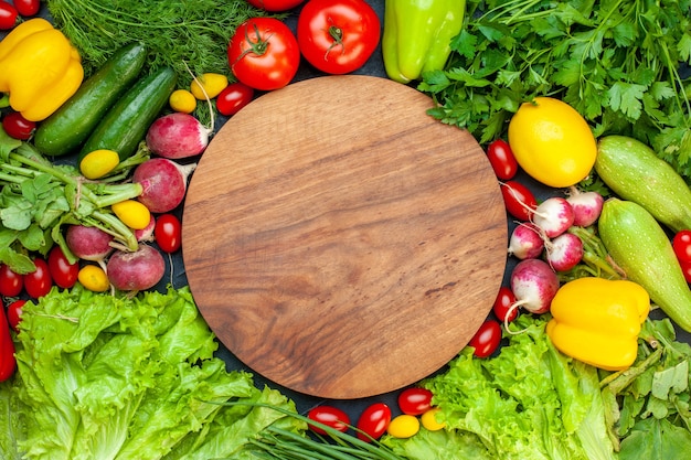 Free Photo top view fresh vegetables tomatoes lettuce radish lemon zucchini parsley cherry tomatoes round wood board in center on dark surface