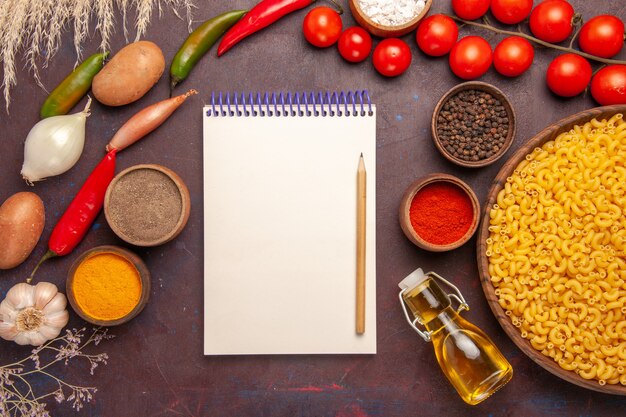 Top view fresh vegetables with different seasonings and pasta on a dark desk