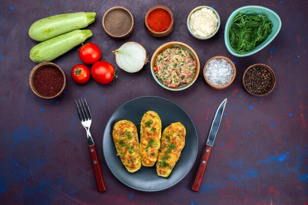 Top view fresh vegetables with greens minced meat cooked squashes and seasonings on dark-purple desk.