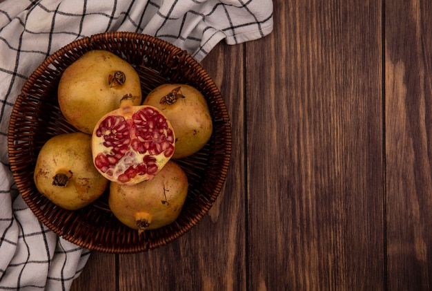 Top view of fresh whole and half pomegranates on a bucket on a checked cloth on a wooden surface with copy space