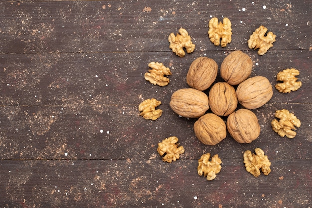 Free photo top view fresh whole walnuts inside shell and cleaned out on brown wood