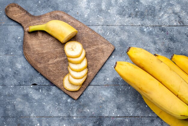 top view of fresh yellow bananas sliced and whole on grey, fresh fruit berry