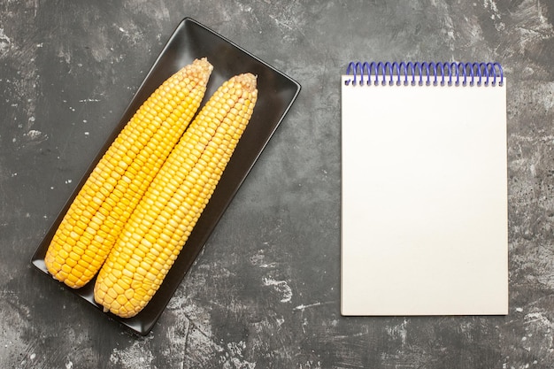 Top view fresh yellow corns inside black pan with notepad on dark background