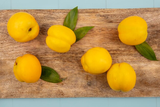 Top view of fresh yellow peaches with leaves isolated on a wooden kitchen board on a blue background