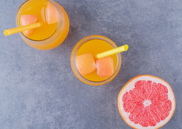 Free photo top view of freshly made orange juice with ripe grapefruit on grey background.