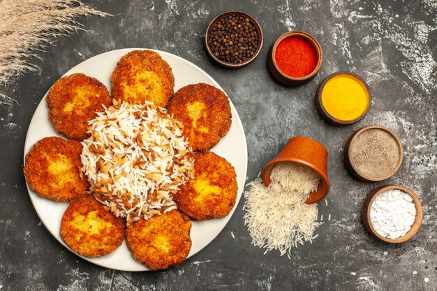 Top view fried cutlets with cooked rice and seasonings on dark surface food meat dish