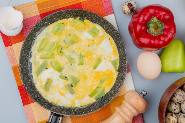 Free photo top view of fried egg on a frying pan with colorful peppers with quail eggs on a wooden bowl on white background