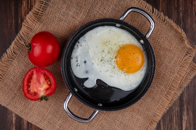 Free photo top view fried egg in a pan with tomatoes on a beige napkin  on a wooden background