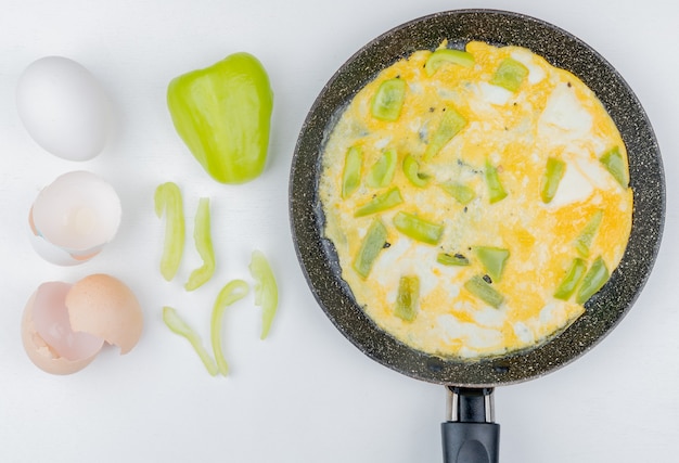 Free photo top view of fried eggs on a frying pan with green bell pepper with cracked egg shells on white background