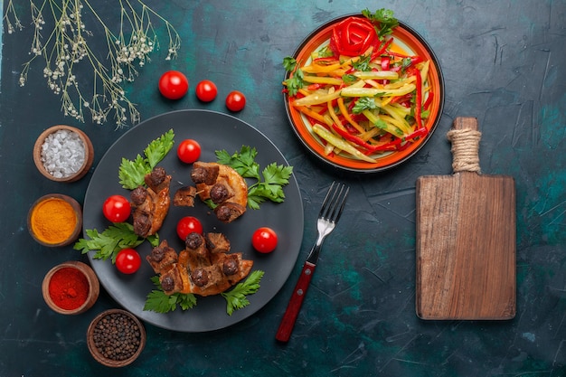 Top view fried meat slices with sliced vegetable salad and seasonings on dark blue desk vegetables food meat health meal