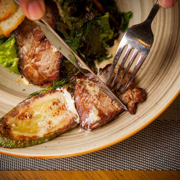 Free photo top view fried meat with fried zucchini and fork and knife and greens in round plate