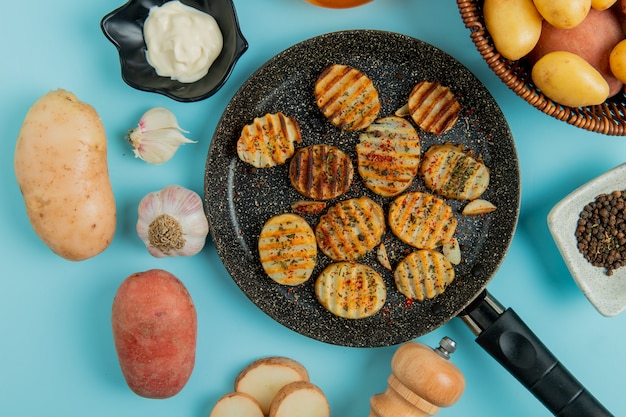 Top view of fried potato slices in frying pan with uncooked ones in basket