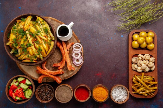 Top view fried potatoes with seasonings and different vegetables on the dark desk