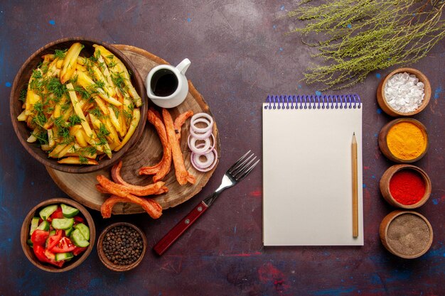 Top view fried potatoes with seasonings and different vegetables on dark surface