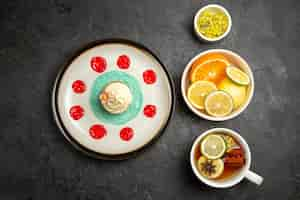 Free photo top view from afar berries and chocolate plate with cupcake with white cream and sauces next to the bowls of herbs and sliced lemons and cup of tea