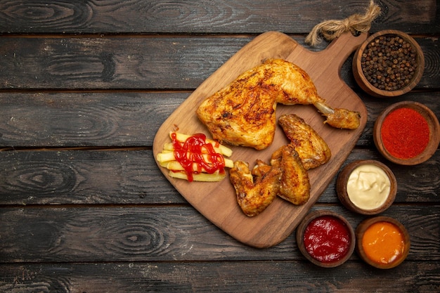 Top view from afar chicken leg and wings bowls of colorful sauces and spices and chicken leg and wings and french fries on the cutting board