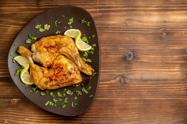 Top view from afar chicken with lemon chicken legs with herbs and lemon in the plate on the left side of the table