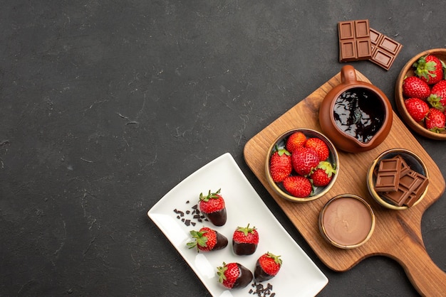 Free photo top view from afar chocolate on board chocolate-covered strawberries on plate next to the cutting board with chocolate cream and strawberries and bars of chocolate