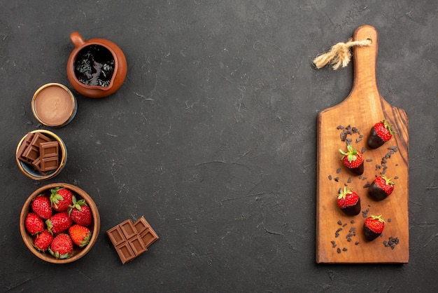 Top view from afar chocolate and strawberries strawberries and chocolate cream on the left and appetizing chocolate-covered strawberries on the wooden cutting board on the right