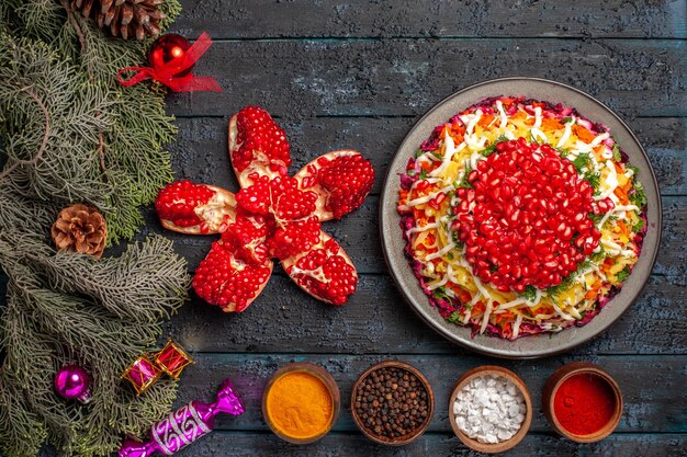 Top view from afar Christmas food Christmas dish with pomegranate bowls of spices pilled pomegranate and spruce branches with Christmas tree toys