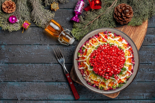 Top view from afar dish in the plate dish with pomegranate carrots on the cutting board next to the bottle of oil fork and tree branches with cones and Christmas tree toys