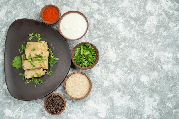 Free photo top view from afar dish in plate stuffed cabbage with herbs in plate next to spices and sour cream on grey table