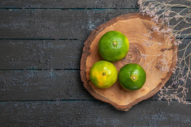 Top view from afar green lime limes on wooden brown board on the right side of the grey table next to branches