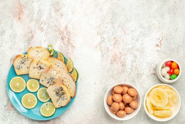 Free Photo top view from afar lemon bread white bread with herbs lemon in the plate next to bowls of candies on the table