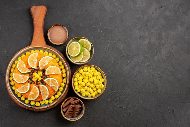 Free photo top view from afar limes and candies appetizing cake with citrus fruits and bowls of different sweets slices of lime on the black table