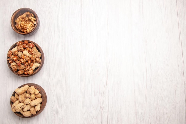 Free photo top view from afar nuts in bowl three bowls of peanuts and walnuts on the left side of the white table