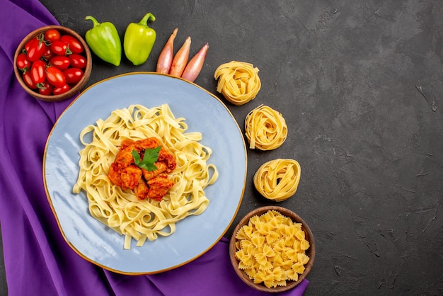 Free photo top view from afar pasta and meat bowl of tomatoes ball pepper onion next to the bowls of pasta and plate of pasta on the purple tablecloth