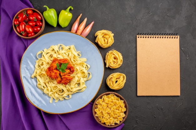 Top view from afar pasta and meat bowl of tomatoes ball pepper onion next to the cream notebook pasta and plate of pasta on the purple tablecloth