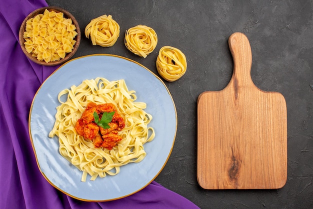 Free photo top view from afar pasta and meat bowls of pasta and plate of pasta gravy and meat on the purple tablecloth next to the cutting board