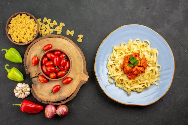 Free photo top view from afar pasta and tomatoes plate of pasta with meat brown bowl of tomatoes on the wooden board pasta and onion bell pepper and garlic on the table