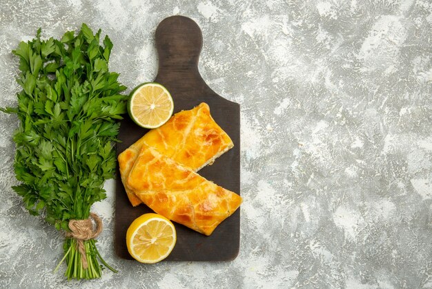 Top view from afar pies herbs cheese lime pies and lemon on the wooden cutting board next to herbs on the left side of the table