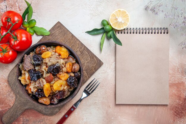 Top view from afar pilaf the cutting board with pilaf fork tomatoes lemon cream notebook