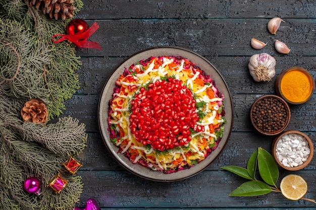 Free photo top view from afar spices on the table tasty dish with pomegranate spruce branches with cones and christmas tree toys bowls of spices garlic oil lemon on the table