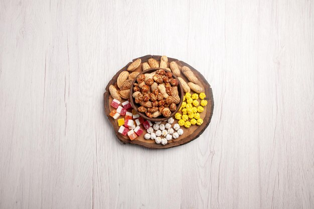 Top view from afar sweets in bowl sweet peanuts in bowl next to the candies on the cutting board on the white table