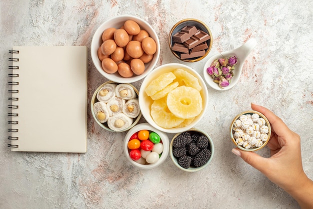 Top view from afar sweets in bowls white notebook next to the bowls of sweets dried fruits and berries in the hand