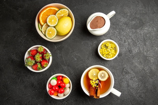 Free photo top view from afar sweets on the table bowls of herbs and strawberries next to the cup of herbal tea with lemon and cinnamon sticks