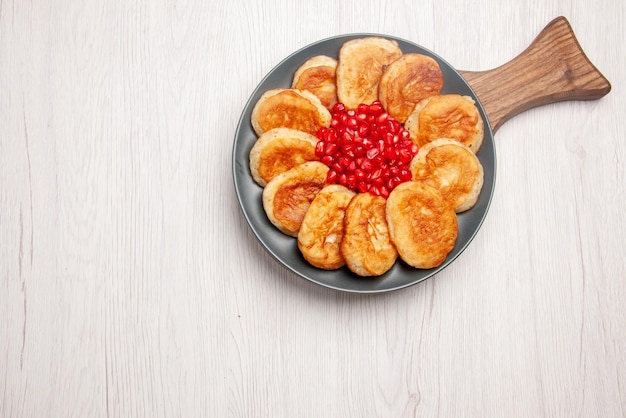 Top view from afar tasty dish plate of appetizing pancakes and pomegranate on the wooden cutting board on the table