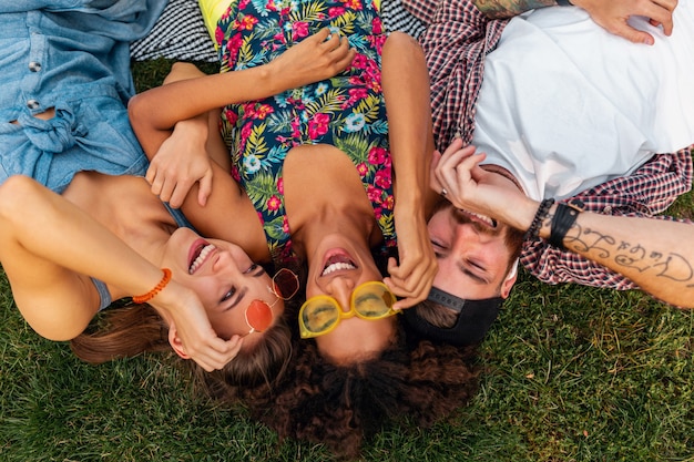 Top view from above on colorful stylish happy young company of friends lying on grass in park, man and women having fun together